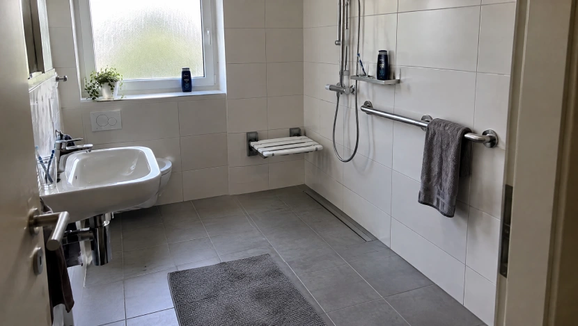 Barrierefreies Bad mit bodengleicher Dusche, klappbarem Duschsitz, Haltegriffen und unterfahrbarem Waschtisch